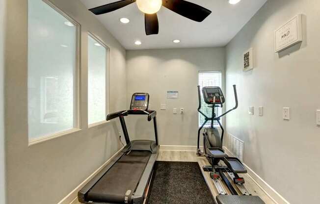 A treadmill and a stationary bike are in a room with a ceiling fan.