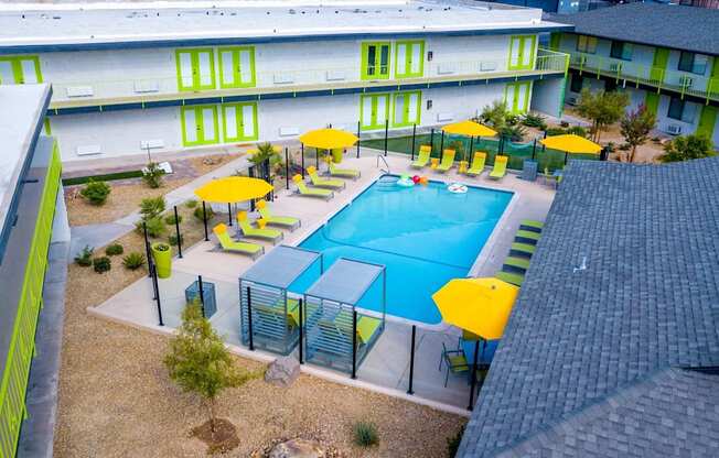 Aerial view of community pool with tall clear fence panels with black fence posts and Fusion Los Vegas apartment buildings with lime green doors.