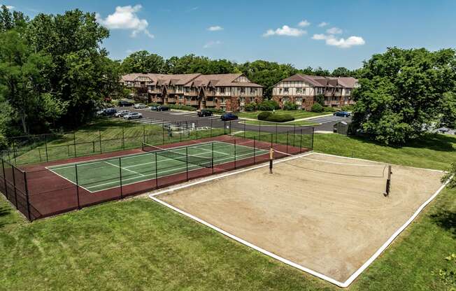 A tennis court surrounded by a fence and trees with apartment buildings in the background
