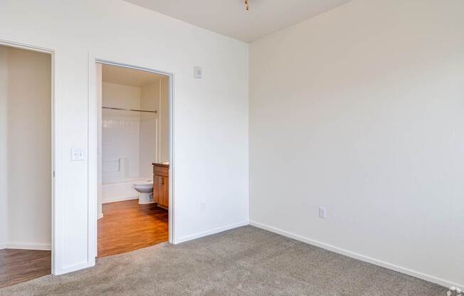 A room with a carpeted floor and a toilet in the other room.