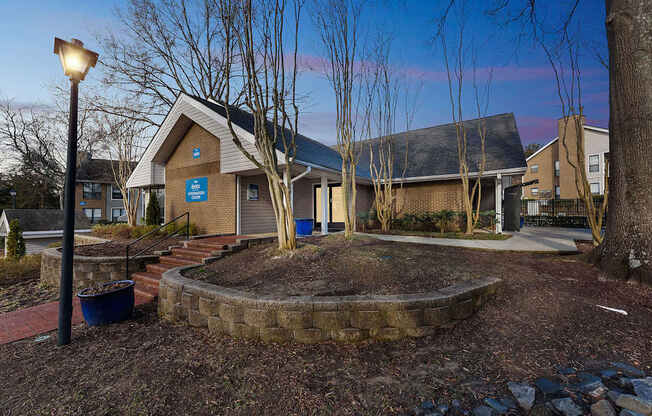 A building with a blue sign on it is surrounded by trees and a small garden.