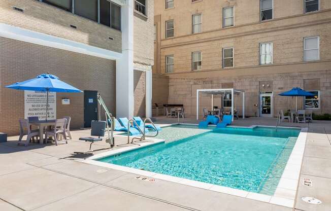 A pool area with a blue umbrella and chairs.