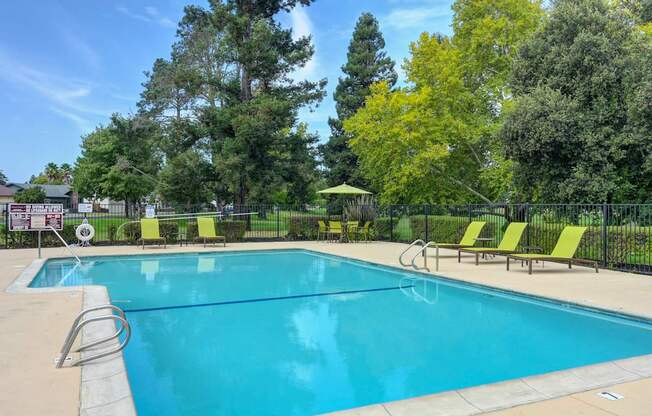 A large swimming pool surrounded by trees and lounge chairs.