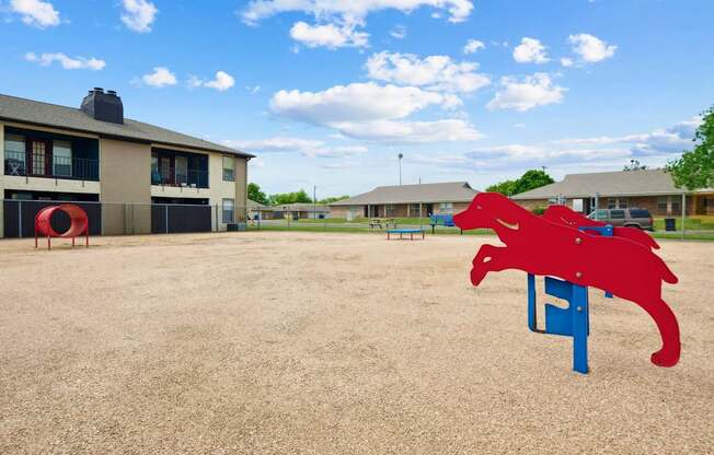 A red dog-shaped dog park equipment sits in the middle of a park at Heritage Square apartments.