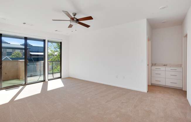 an empty living room with a ceiling fan and a balcony