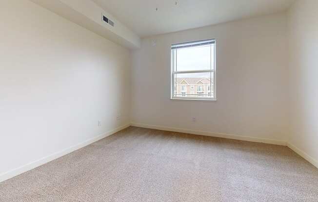 Empty bedroom with carpeted floor and a window at The Reserve at Destination Pointe apartments, Grimes, IA