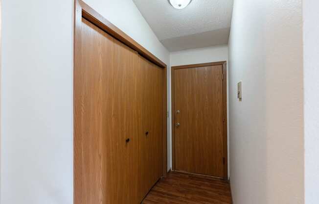 an empty hallway with a wooden door and a closet. Fargo, ND Rosegate Apartments