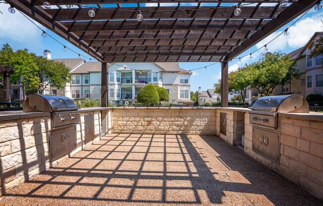 a pergola with two barbecue grills and a stone wall