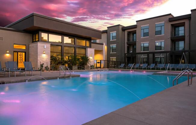 A swimming pool in front of a building with a sunset in the background.