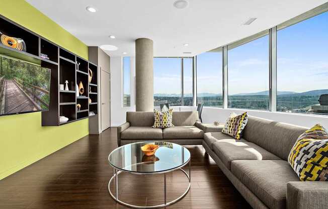 A modern living room with a glass table and a grey couch.