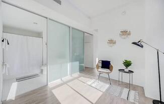 a white bathroom with a glass shower and a chair