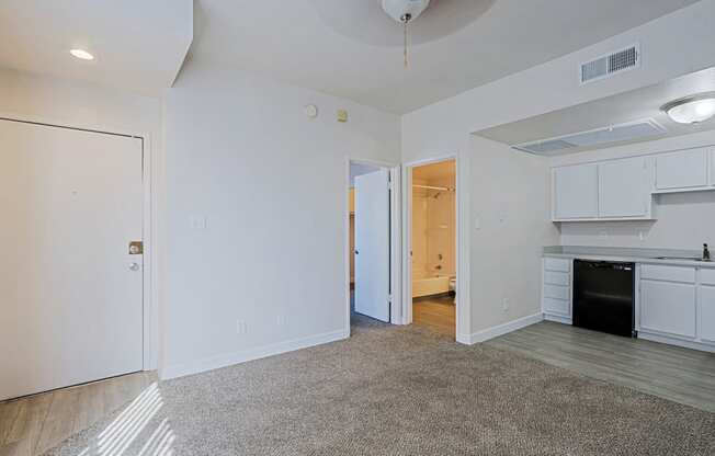 the living room and kitchen of an apartment with white walls and wood flooring