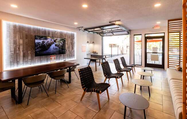 a lounge room with tables and chairs and a tv on the wall