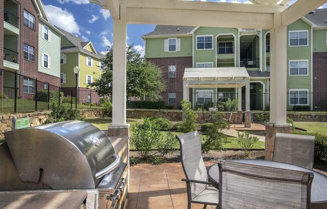 Dog-Friendly Apartments in Tyler, TX - Covered Community BBQ Area with Counter Space, Table and Seating, and Lush Landscaping.