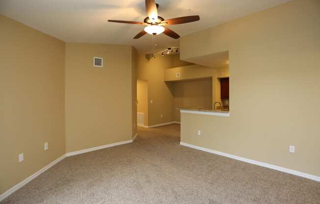 an empty living room with a ceiling fan and a kitchen