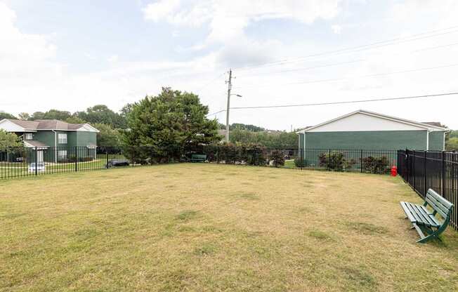 A large grassy field with a bench and a fence.
