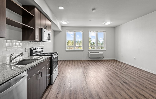Studio kitchen with stainless-steel dishwasher, oven, range, microwave, and refrigerator, granite countertops and white subway-style backsplash featuring large windows