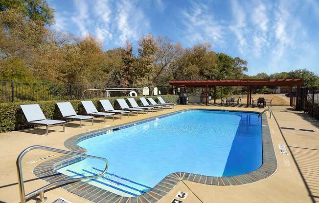 View of gated second community pool with lounge chairs, pergola covering grilling station with counters to meal prep, and seating.