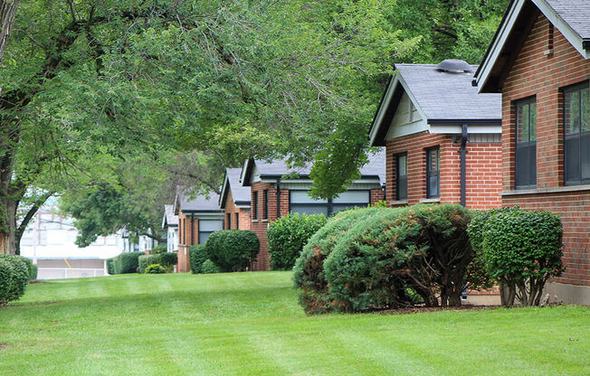 a row of houses on a green lawn with trees and bushes