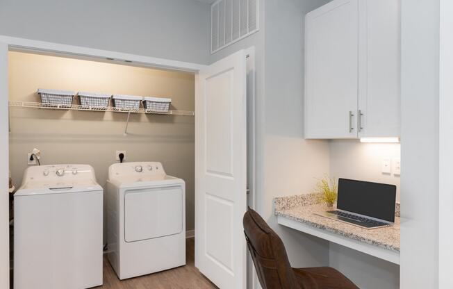 a desk with a laptop and a washer and dryer in a laundry room