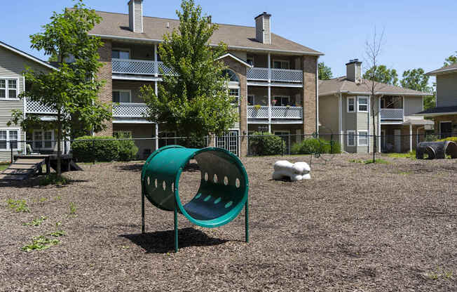 A green playground slide in front of apartment buildings.