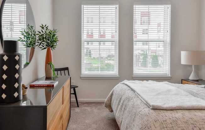 A bedroom with a bed, a dresser, and a window with blinds.