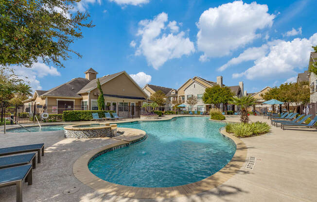 A large outdoor swimming pool surrounded by lounge chairs and trees.