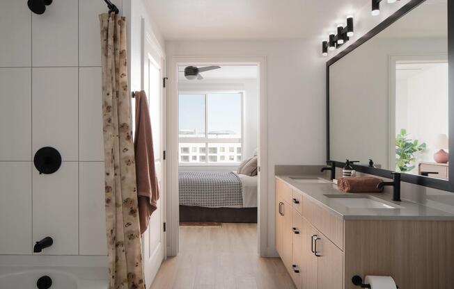 A bright bath with dual sinks, matte black fixtures, and a seamless flow into the bedroom beyond.