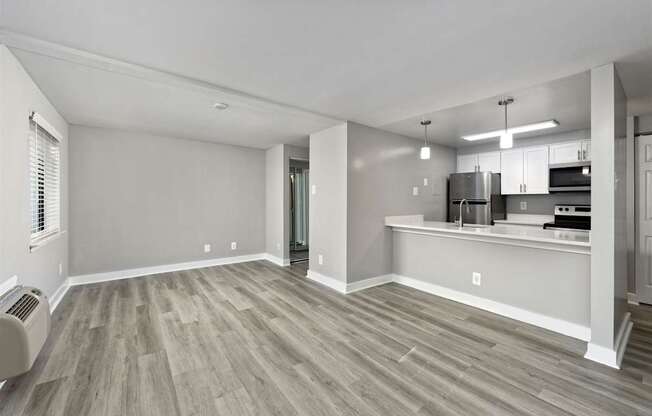 A spacious living room with a wood floor and a kitchen area in the background.