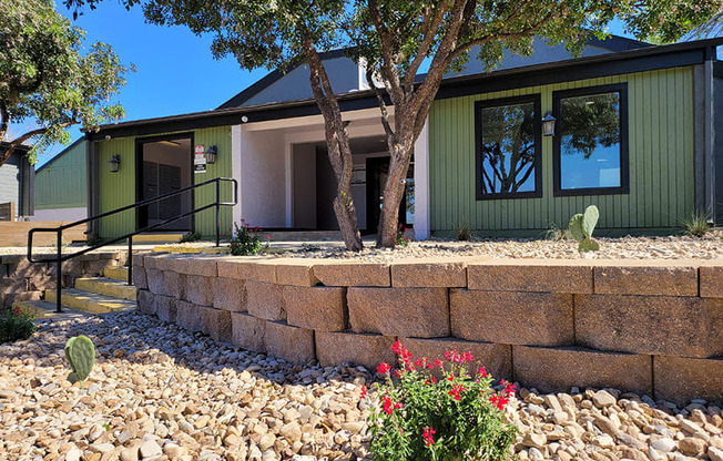 a house with a stone retaining wall and a tree in front of it at Ivy Plains at Brooks Apartments, Texas