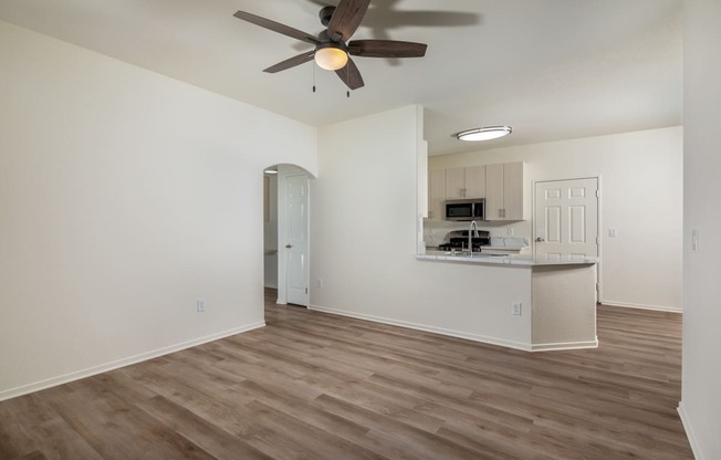 an empty living room with a ceiling fan and a kitchen