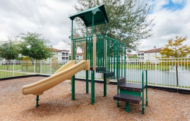a playground with a slide and bench in front of a body of water
