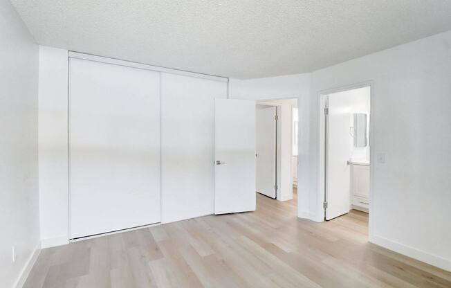 A room with white walls and wooden flooring with three white doors.
