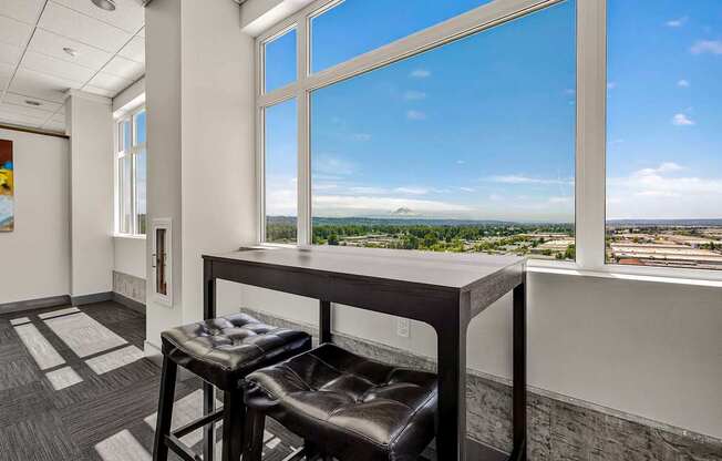 A room with a table and two chairs in front of a large window with a view of the city.