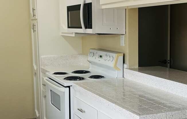 Kitchen with white cabinets and appliances, plank style flooring, and server bar at Plaza Verde Apartments in Escondido, California.