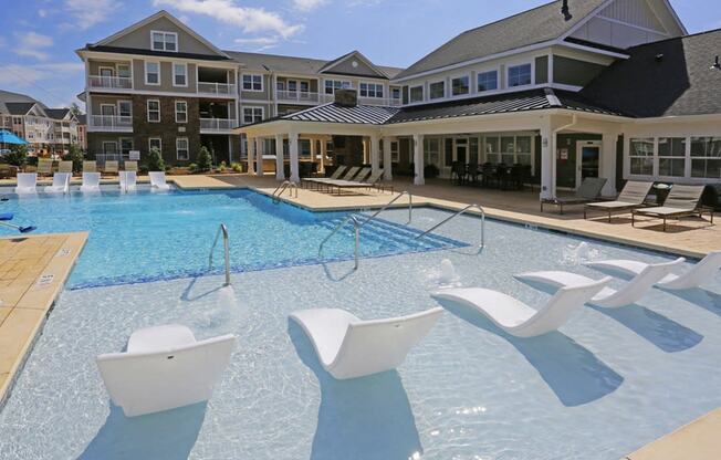 a large swimming pool with white chairs in front of an apartment building