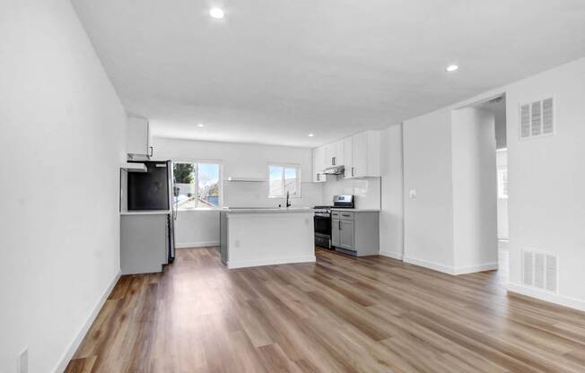 an open kitchen and living room with white walls and wood floors