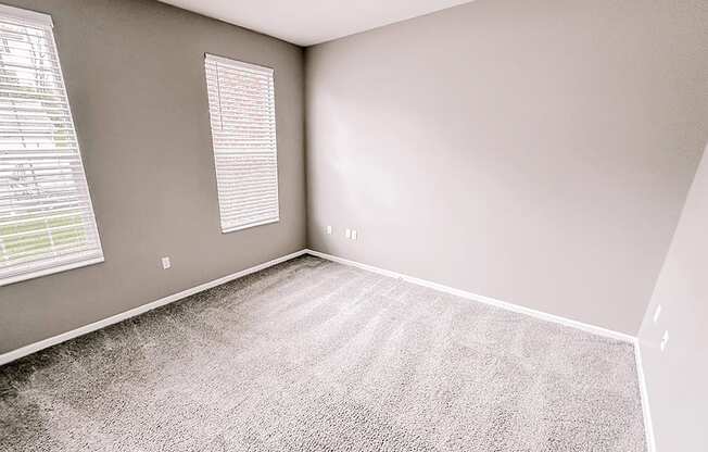 an empty room with carpet and two windows
