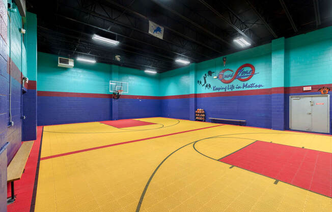 a basketball court in a gym with a blue wall and a red and yellow floor