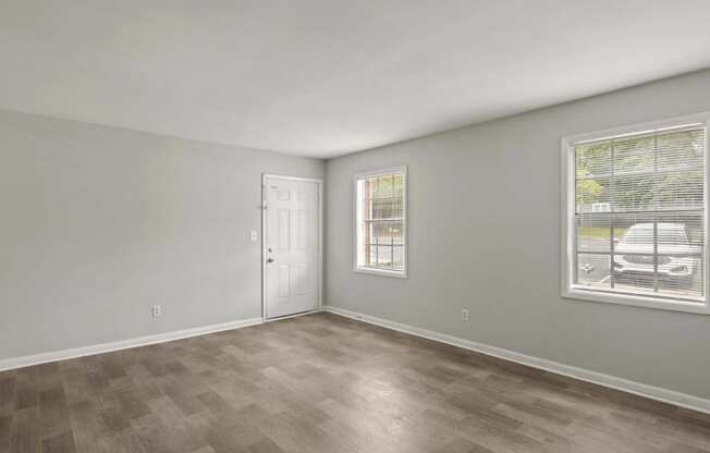 the spacious living room of an apartment with a white door and window