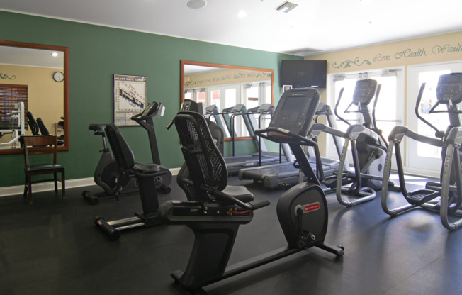 A gym with a green wall and a row of treadmills.,A gym with a green wall and a row of treadmills.
