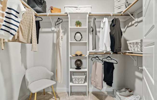 A white closet with clothes and a chair.
