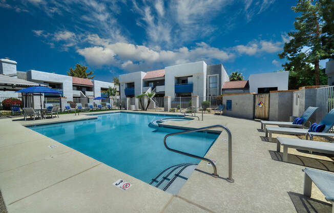 a swimming pool with lounge chairs and umbrellas at the whispering winds apartments in pearland