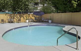 Fenced pool area with patio seating and an umbrella at Casa Blanca Apartment Homes, Everett, WA, 98204