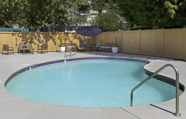 Fenced pool area with patio seating and an umbrella at Casa Blanca Apartment Homes, Everett, WA, 98204