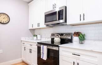 A white kitchen with a black stove top oven and a microwave above it.