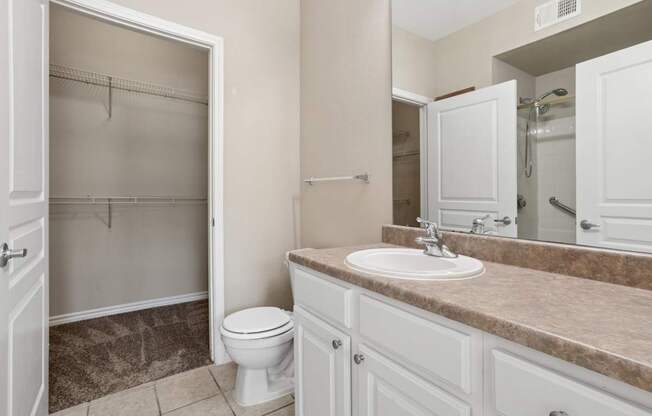 Edinburgh bathroom with a toilet, sink, and mirror at Encore at Buckingham Apartments in Richardson, TX