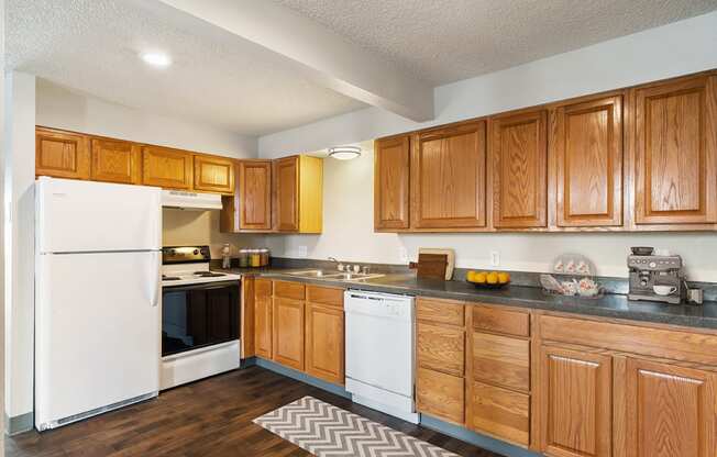 A spacious l-shaped kitchen with top and bottom wood cabinets, hardwood floors, and white appliances.at Wildflower, Kennewick