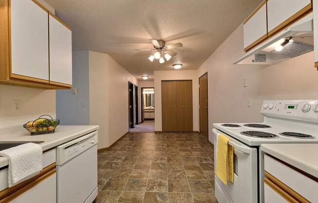 A kitchen with white appliances and white cabinets and a ceiling fan. Fargo, ND Eagle Run Apartments.