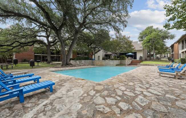 A pool surrounded by trees and chairs.